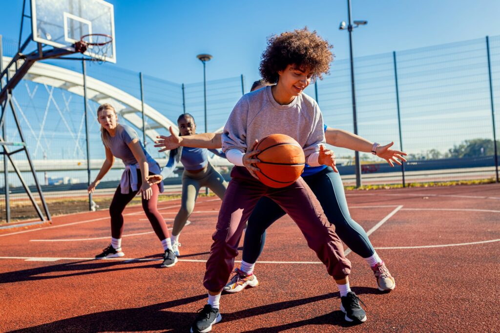 Diverse group of young woman having fun playing recreational basketball outdoors.